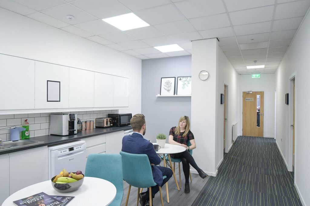 Two people talking at a small table in a kitchen and corridor at Hope Park