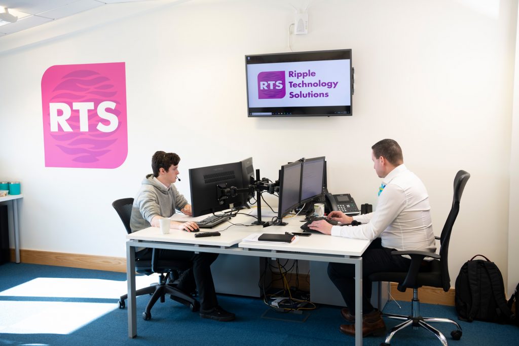 The Ripple Technology Solutions team working at their desks under an RTS sign