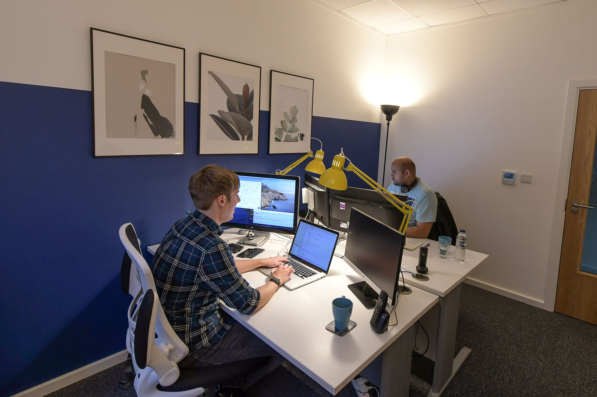Two people working at desks with large monitors in a small office at Hope Park
